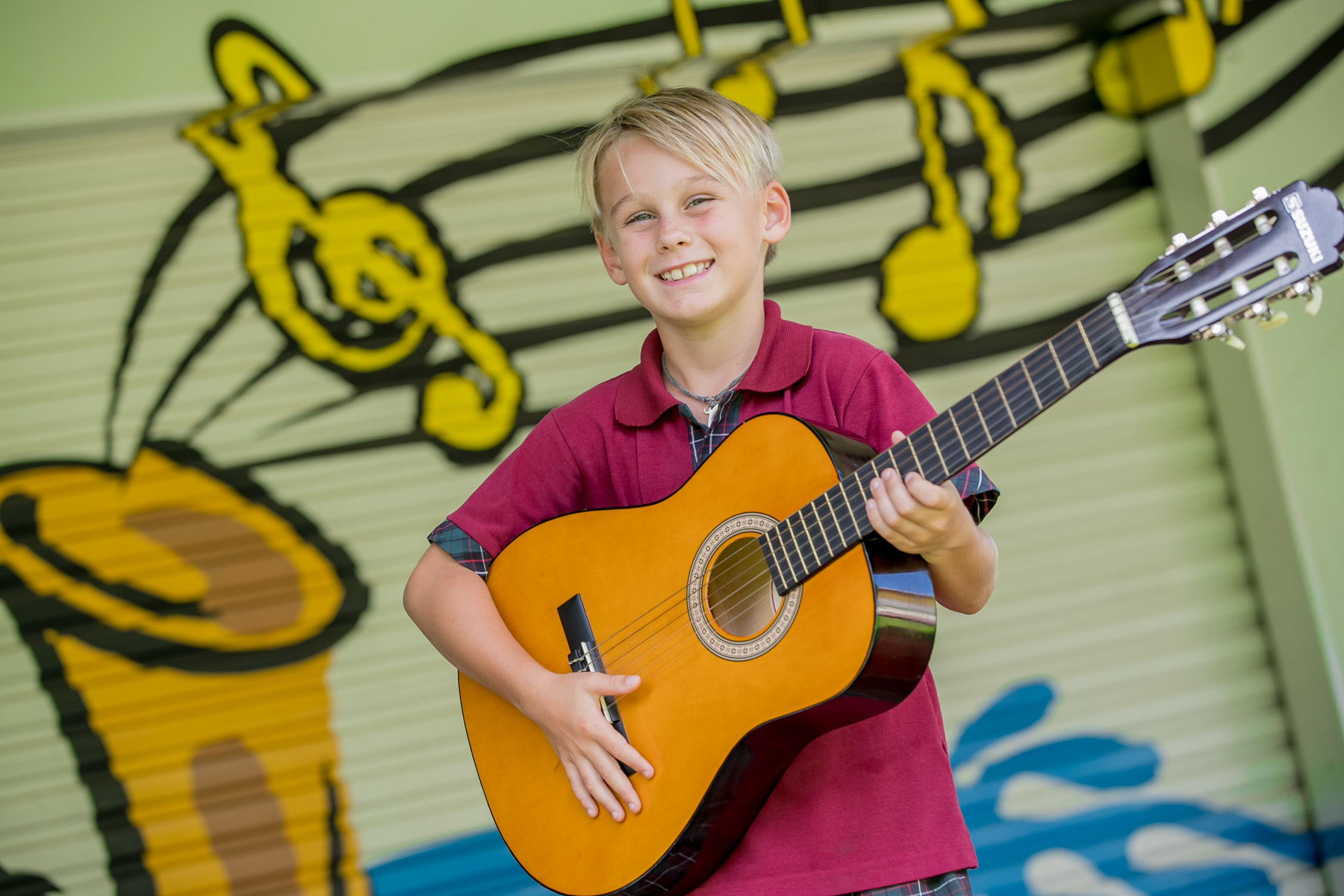 Student holding a classical guitar in front of a mural with musical notes.