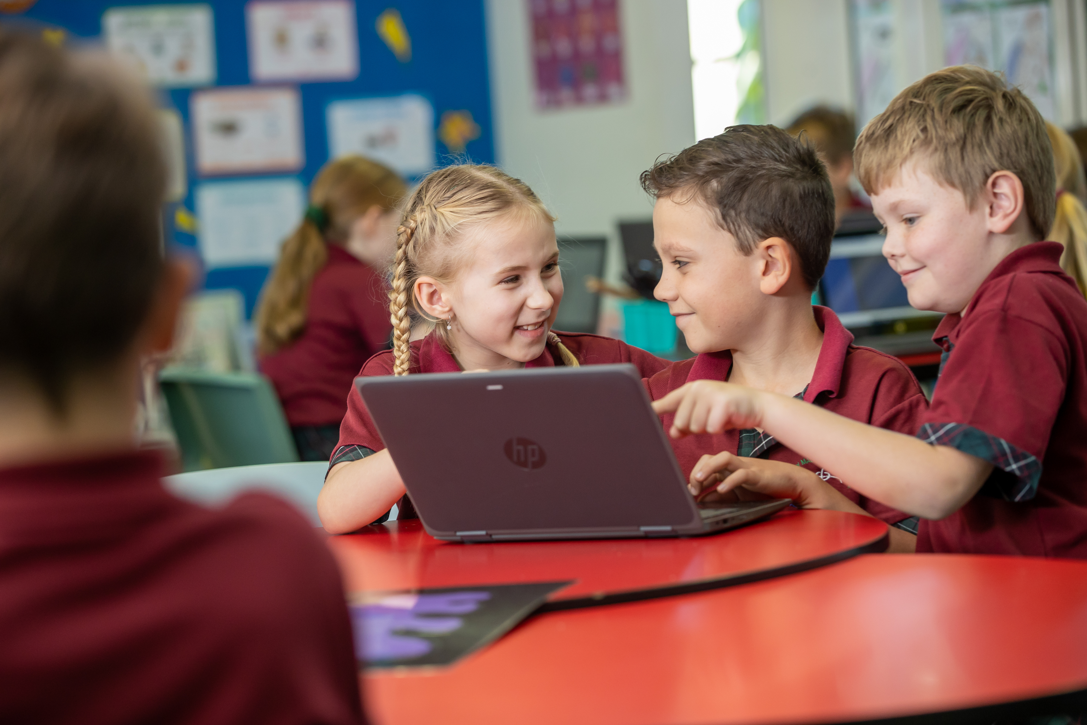 Primary school students working together at a table using a laptop in a classroom.