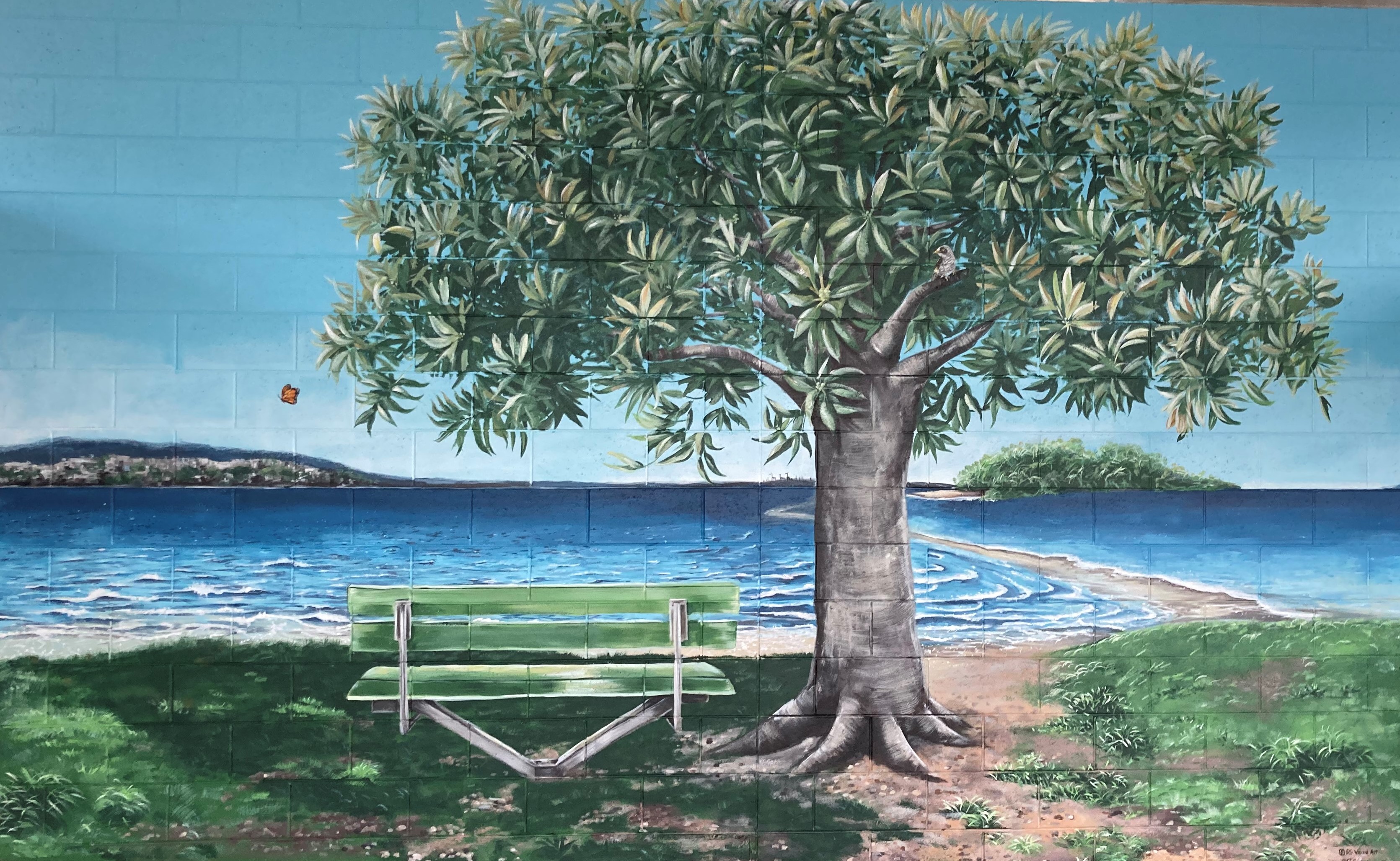 Painted mural of a large tree beside a green bench overlooking the ocean, with distant islands and shoreline in the background.